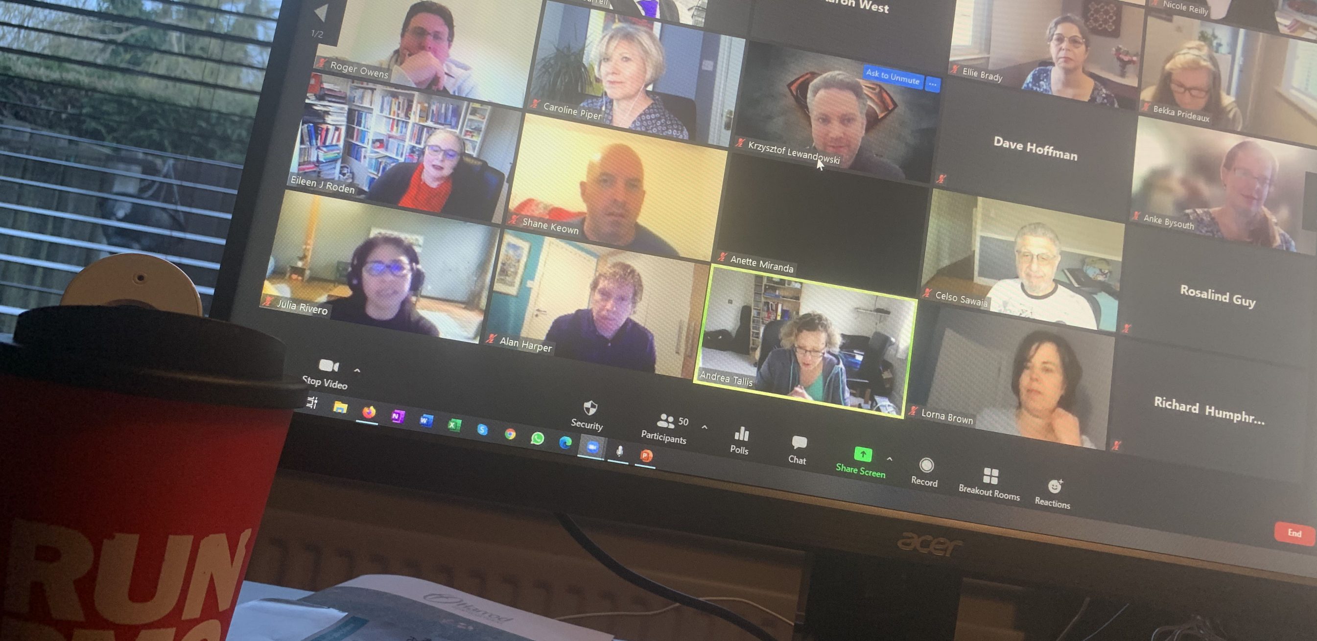 A desk with a PMO branded mug. A Monitor on the desk shows people in a zoom call.